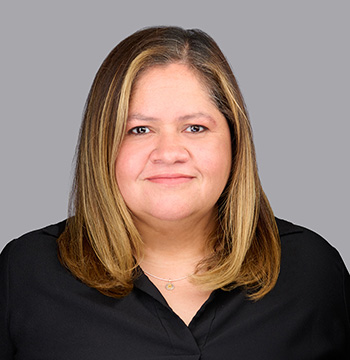 A woman with straight, shoulder-length light brown hair wearing a black top poses against a plain gray background.