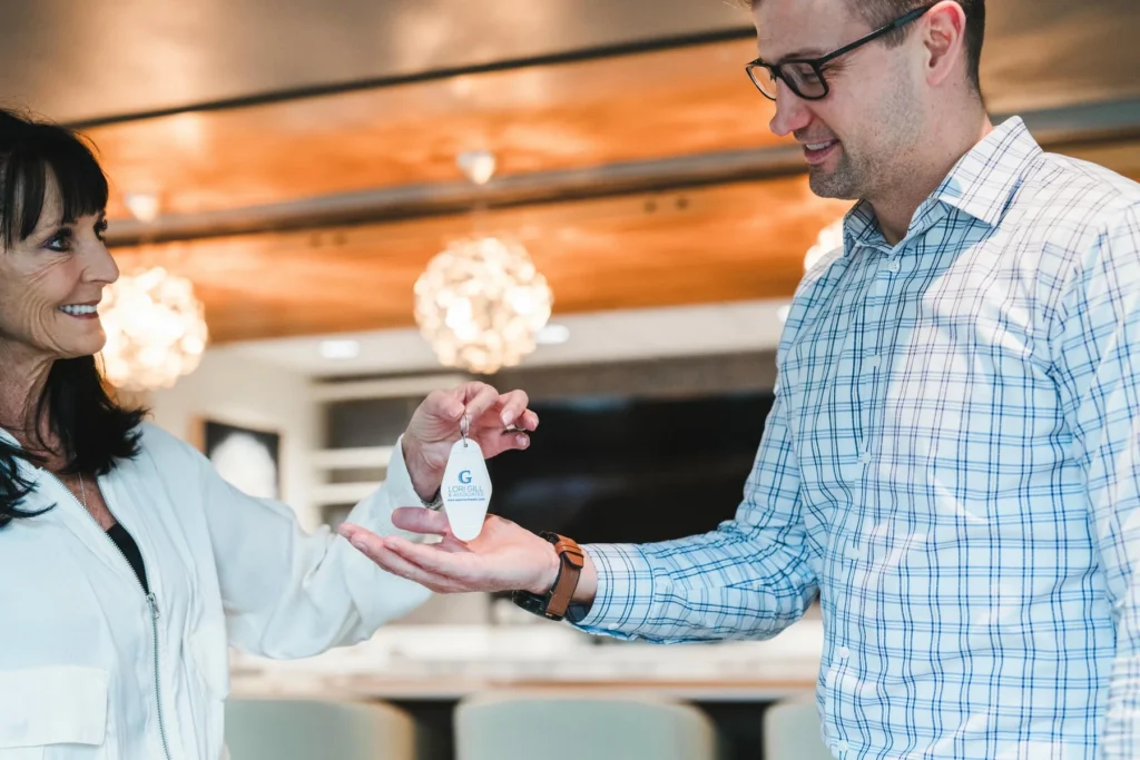A woman hands a keychain with a room key to a man in a modern, well-lit interior space.