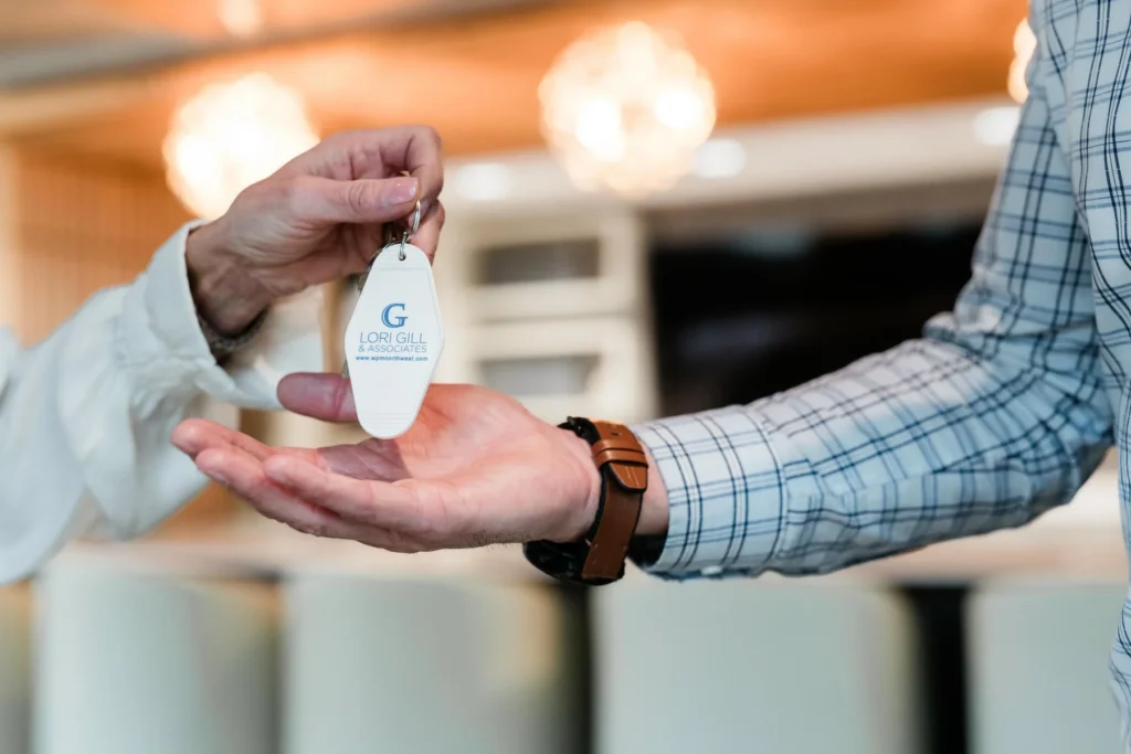 A person hands over a keychain with the Lori Gill & Associates logo to another person wearing a plaid shirt and brown watch.