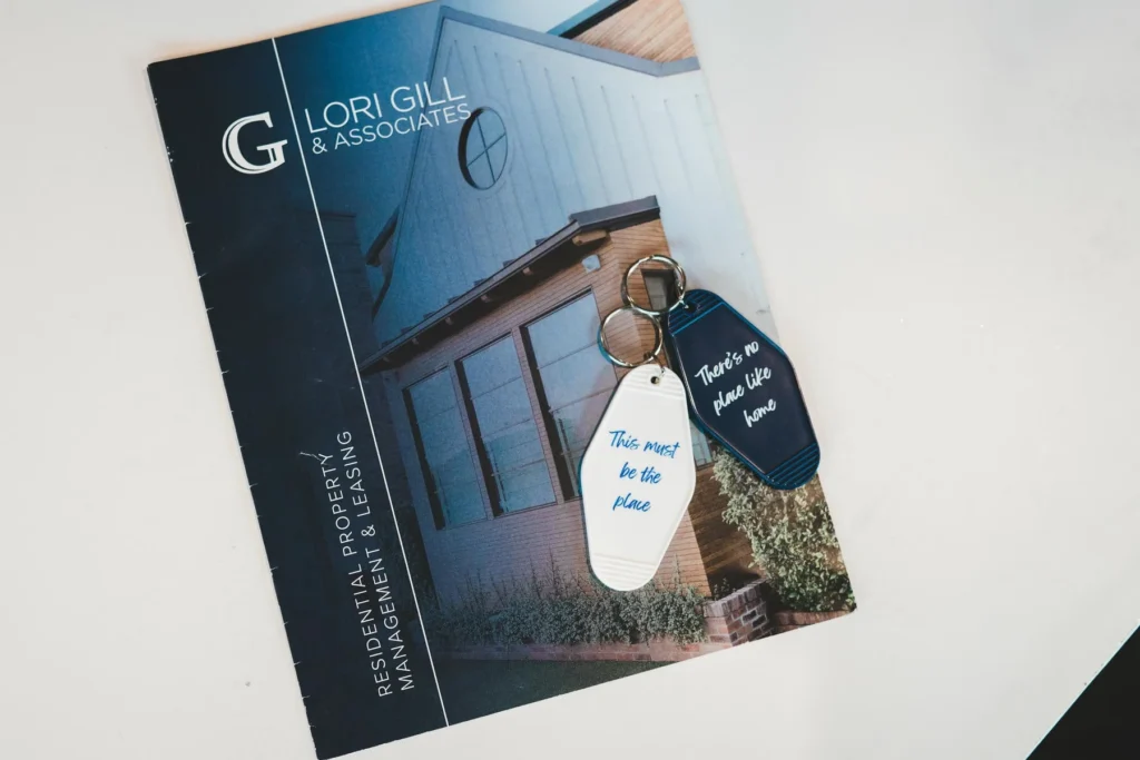 A brochure for Lori Gill & Associates with two keychains on top, one reading This must be the place and the other Theres no place like home.