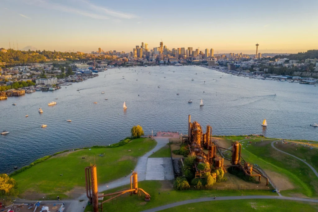 Aerial view of Gas Works Park with its industrial structures in the foreground, Lake Union in the middle, and downtown Seattle skyline and Space Needle in the background.