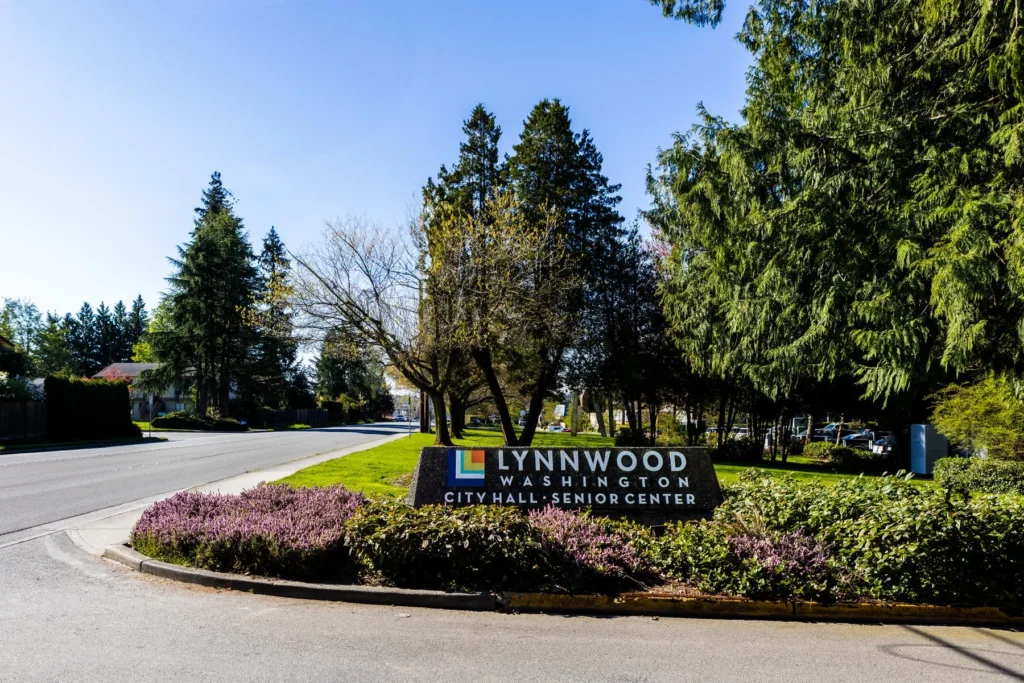A roadside sign reads Lynnwood Washington City Hall Senior Center, surrounded by landscaping and trees on a sunny day.