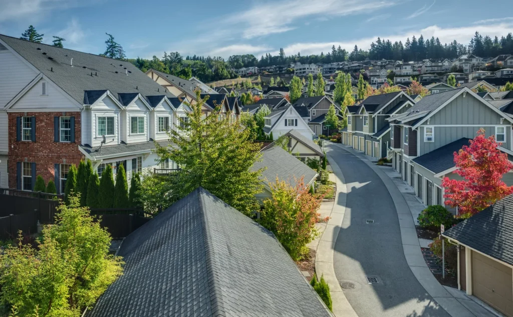 A suburban neighborhood with modern houses, tree-lined streets, and a curved road under a blue sky with scattered clouds.
